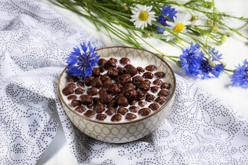 Obraz na płótnie Canvas Breakfast cereal, Chocolate cereals in milk with cornflower flower on a natural napkin , concept of healthy nutrition for children, soft focus