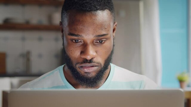 Anxious afro-american guy looking at laptop screen at home