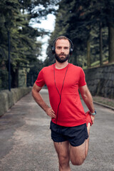 Sporty adult man making pause after jogging and exercising in the park.