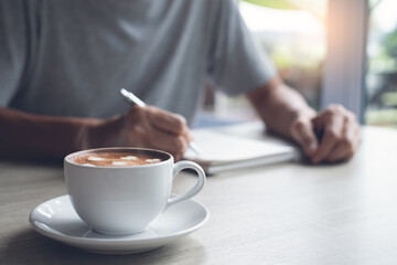 Casual man writing notes on paper notebook in coffee shop