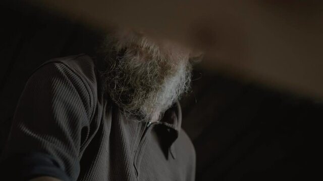 Male carpenter with a gray beard, puts a board on a workbench before processing it with a planer. An elderly artisan will carry out his work intently in a workshop. Handwork of the master.