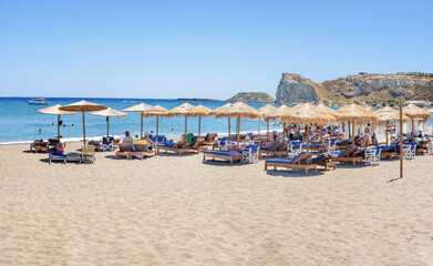 Fototapeta na wymiar Holiday-makers, sun beds and umbrellas on Stegna beach (RHODES, GREECE)