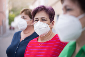  3 older women with face mask on the street and one of them looking at the camera