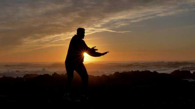 Men warrior monk practicing silhouette tai chi karate kung Fu on the rocky stones horizon at sunset or sunrise. Art of self-defense. Silhouette on a background of dramatic epic waves at pacific coast