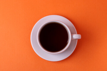 a white ceramic cup with black tea on orange background. minimalism style