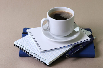 black espresso in a cup and notebooks and a pen on light pastel tones background
