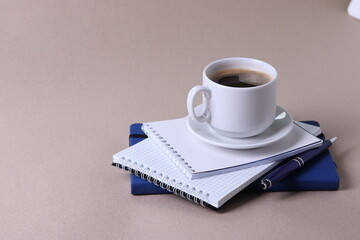black espresso in a cup and notebooks and a pen on light pastel tones background