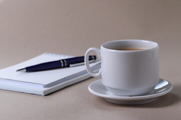 black espresso in a cup and notebooks and a pen on light pastel tones background