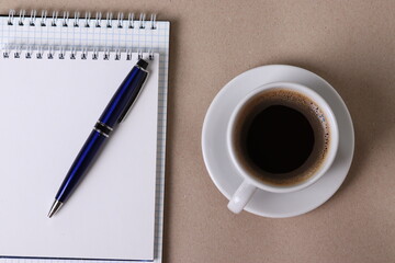 black espresso in a cup and notebooks and a pen on light pastel tones background