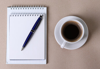 black espresso in a cup and notebooks and a pen on light pastel tones background