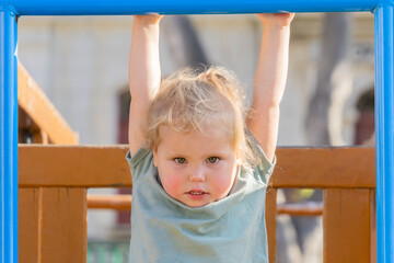 Little girl hanging horizontal bar in playground