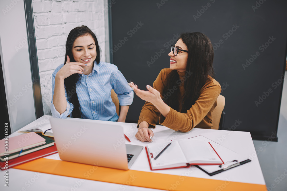 Poster cheerful female colleagues having fun during working process on project talking and joking with each