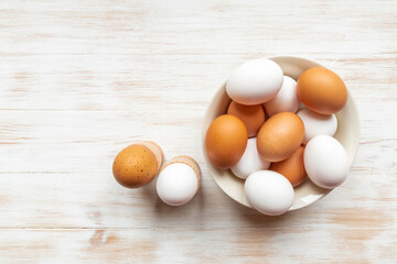 Free-range organic brown and white eggs in bowl and boiled eggs in holders on wooden background