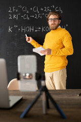 Bearded chemistry teacher in casualwear pointing at chemical formula