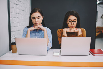 Female students concentrated on watching tutorial learning language via online course on laptops, thoughtful antisocial hipster girls contemplatively read information from netbooks prepare for exams © BullRun
