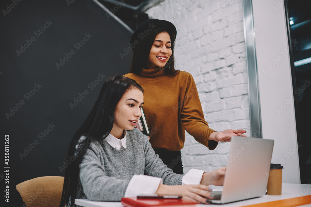 Poster smiling young woman pointing on laptop computer laughing on web page content while spending time wit