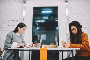 Antisocial female students using technology during learning process in college campus ignoring talking to each other, skilled employees concentrated on their working process using modern devices.