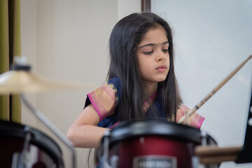 Fototapeta na wymiar British Indian girl practices the drums wearing a traditional saree or sari. 