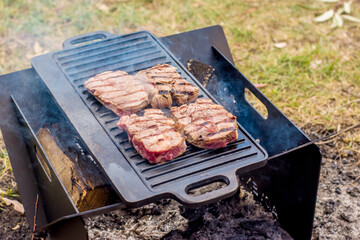 Beef steaks grilling on a cast iron plate on a camp fire. Campfire cooking. Outdoor BBQ.