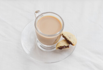 homemade butter cookies filled with chocolate flavored cream next to a full glass of instant coffee with milk, against a wooden background