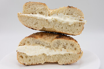 Cut In Half Toasted Sesame Seed Bagel with Cream Cheese on a White Plate with a White Background