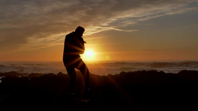 Men warrior monk practicing silhouette tai chi karate kung Fu on the rocky stones horizon at sunset or sunrise. Chakra practice.Silhouette on a background of dramatic epic waves at pacific coast
