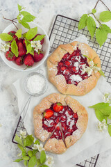 Two biscuits with strawberries or an open pie with jasmine flowers on a light background and paper with a cut piece and a bowl with strawberries and icing sugar. Vertical layout