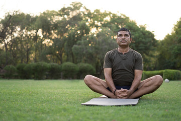 Mid-aged Man doing yoga in a park covered with trees on International Yoga Day.