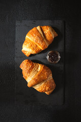 Fresh golden croissants on dark slate board. Top view