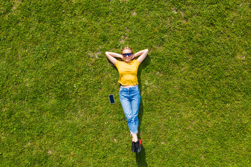 Aerial view. Young girl lying and resting on lawn on sunny day in park on grass. Above view. Woman...