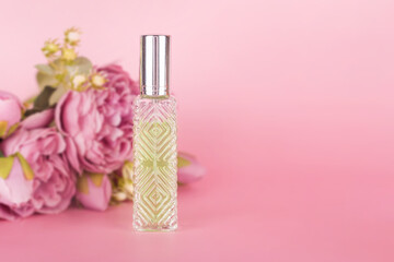 Transparent perfume bottle with bouquet of peonies on pink background. Aromatic essence bottle with spring flowers. Perfumery, cosmetics, fragrance collection. Free space for text