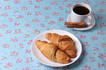 a white ceramic cup of coffee and a saucer with cinnamon sticks on vintage pattern textile surface