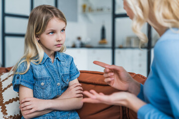 Little girl looking sad while her mother scolding her sitting on couch at home - Powered by Adobe