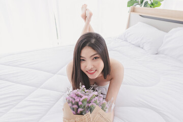 Obraz na płótnie Canvas Asian beautiful girl wearing casual clothes and Lying on the bed and Smile looking camera with Purple flower bouquet Happily