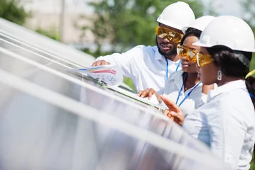 Foto op Canvas African american technician checks the maintenance of the solar panels. Group of three black engineers meeting at solar station. © AS Photo Family