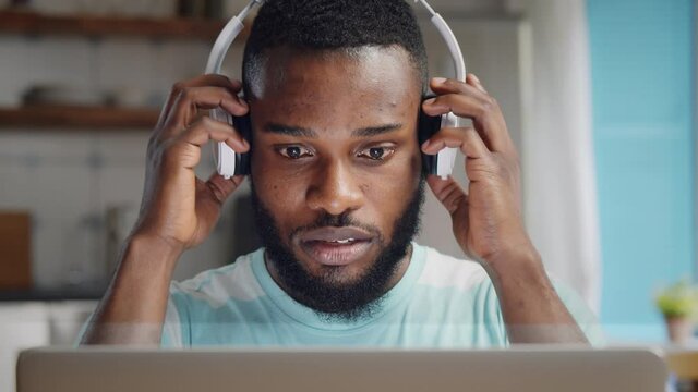 African student guy in headphones using laptop at home