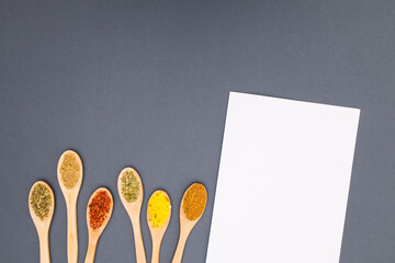 Different spices in wooden spoons and white paper for recipe 