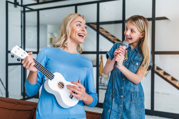 Mom and cute little girl with microphone singing together and playing ukulele