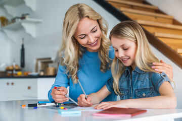 Beautiful woman helping her child daughter doing homework at home kitchen