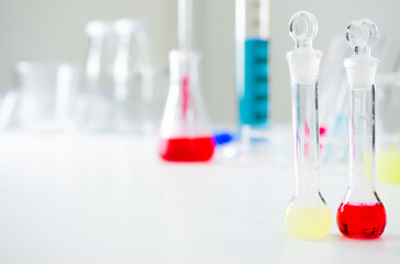 2 sci-science vials with corks placed next to each other, with red and light green water inside On the white table Behind there is much experimental equipment. In the white lab with copy space