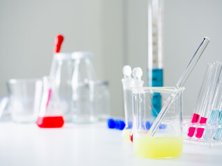 Clear glass beaker With light green water and a glass rod inside Behind and besides, there are many more instruments placed on a white table in the laboratory. There is a copy space concept.