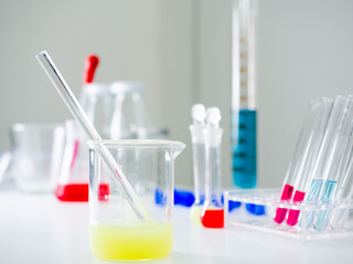 Clear glass beaker With light green water and a glass rod inside Behind and besides, there are many more instruments placed on a white table in the laboratory. There is a copy space concept.