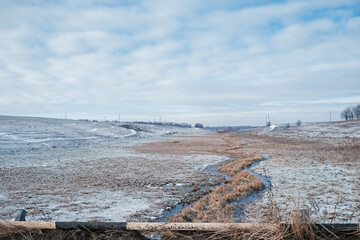 wintry winding creek, little bridge and snow covered field landscape