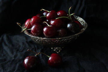 Fresh sweet ripe cherries on rustic plate on black background. Close up.