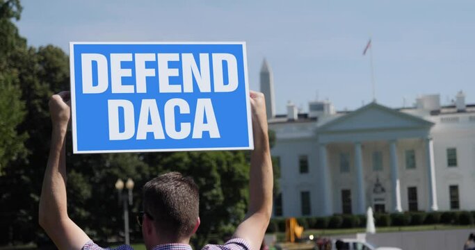 A man holds a DEFEND DACA protest sign outside of the White House. 