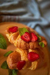 Croissants on a wooden board with strawberries. Perfect breakfast. Crispy croissants with berries and mint.