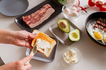 Hands of young woman with knife spreading dairy product on toast over table