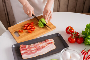 Hands of young housewife cutting fresh avocado and tomatoes on chopping board