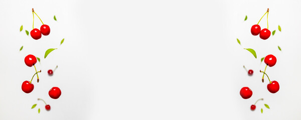 Falling organic fresh ripe cherries with green leaves frame isolated on white background.