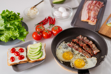 Appetizing vegetarian sandwiches, fried eggs and bacon and fresh vegs on table